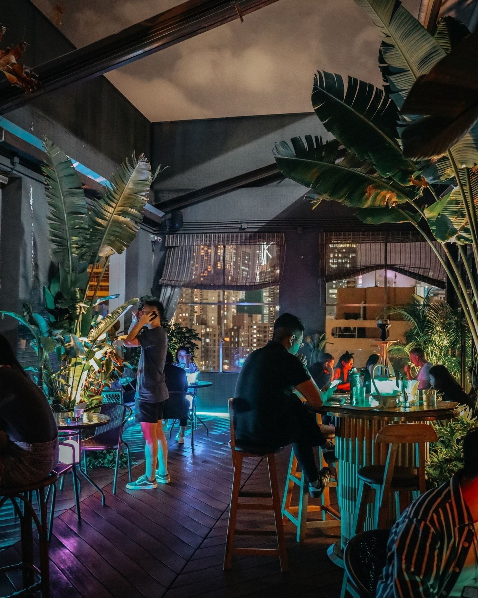 The Tiki-inspired interior of Ohana, with guests sitting at tables, tropical plants and purple and blue lighting